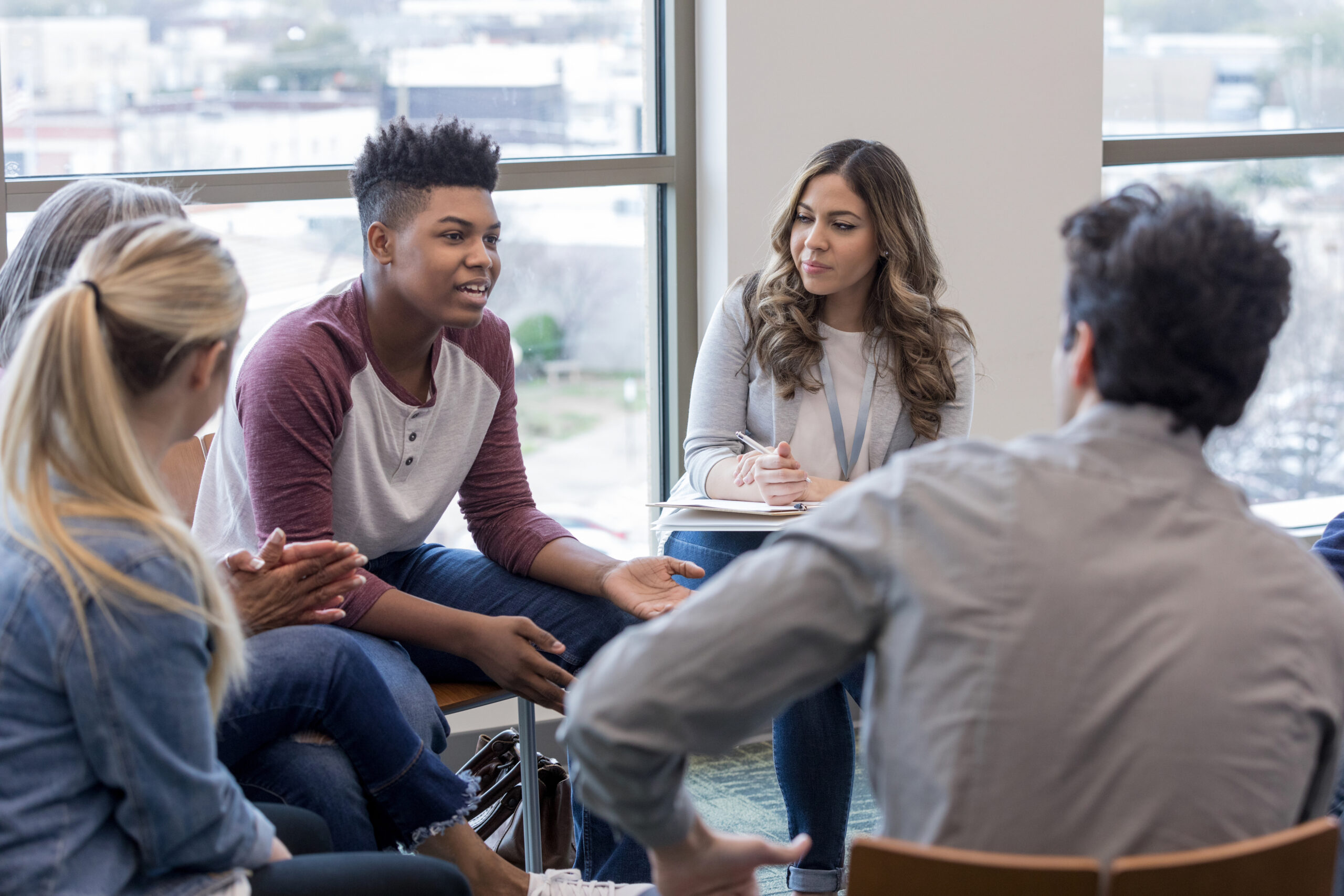 Group of teens sitting in a circle talking to a counselor.